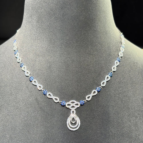 A silver-toned necklace with blue gemstone accents and a teardrop pendant, displayed on a gray velvet jewelry bust against a dark background.
