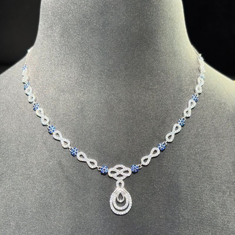 A silver-toned necklace with blue gemstone accents and a teardrop pendant, displayed on a gray velvet jewelry bust against a dark background.