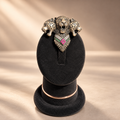 A three-headed leopard pendant with a heart-shaped center featuring pink and green stones, displayed on a black velvet jewelry stand against a warm beige background.